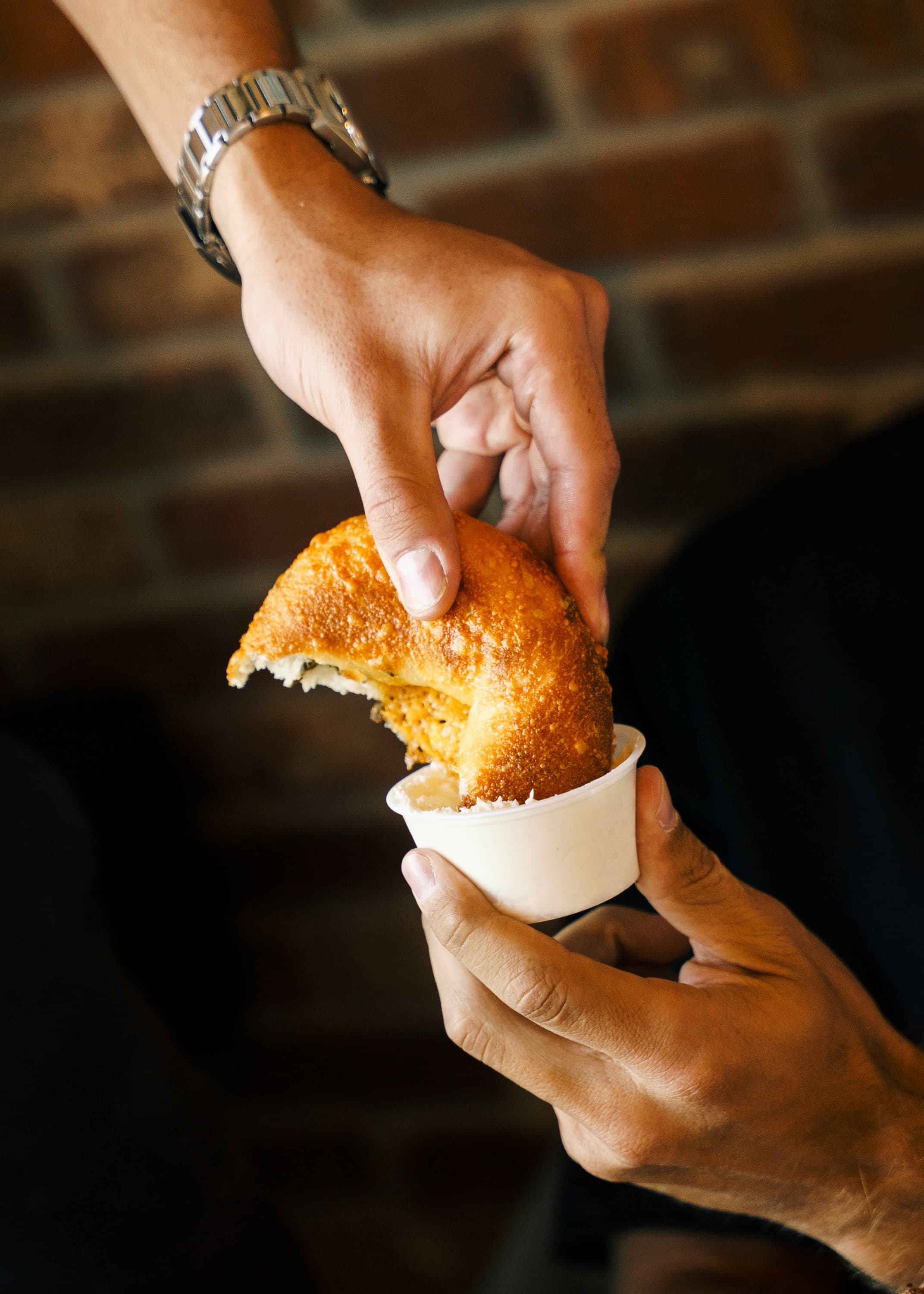 A fresh bagel being dipped into house-made schmear